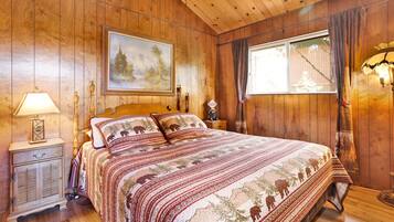 Een slaapkamer met houten lambrisering, een bed, nachtkastje, lamp, schilderij en een raam met gordijnen.