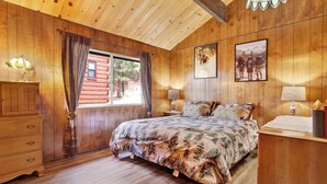 Una habitación acogedora de madera con una cama, dos mesitas de noche y un aparador.