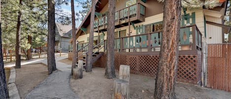Un refugio rústico con varios balcones, suelo de tierra y árboles circundantes.