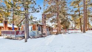 A cabin with a stone chimney, wooden exterior, and a porch with a railing. - Lakeside 109 (Big Bear Lake)