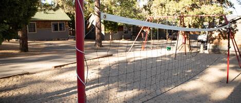 Una rete da pallavolo in una zona sabbiosa, con alberi e un edificio sullo sfondo.