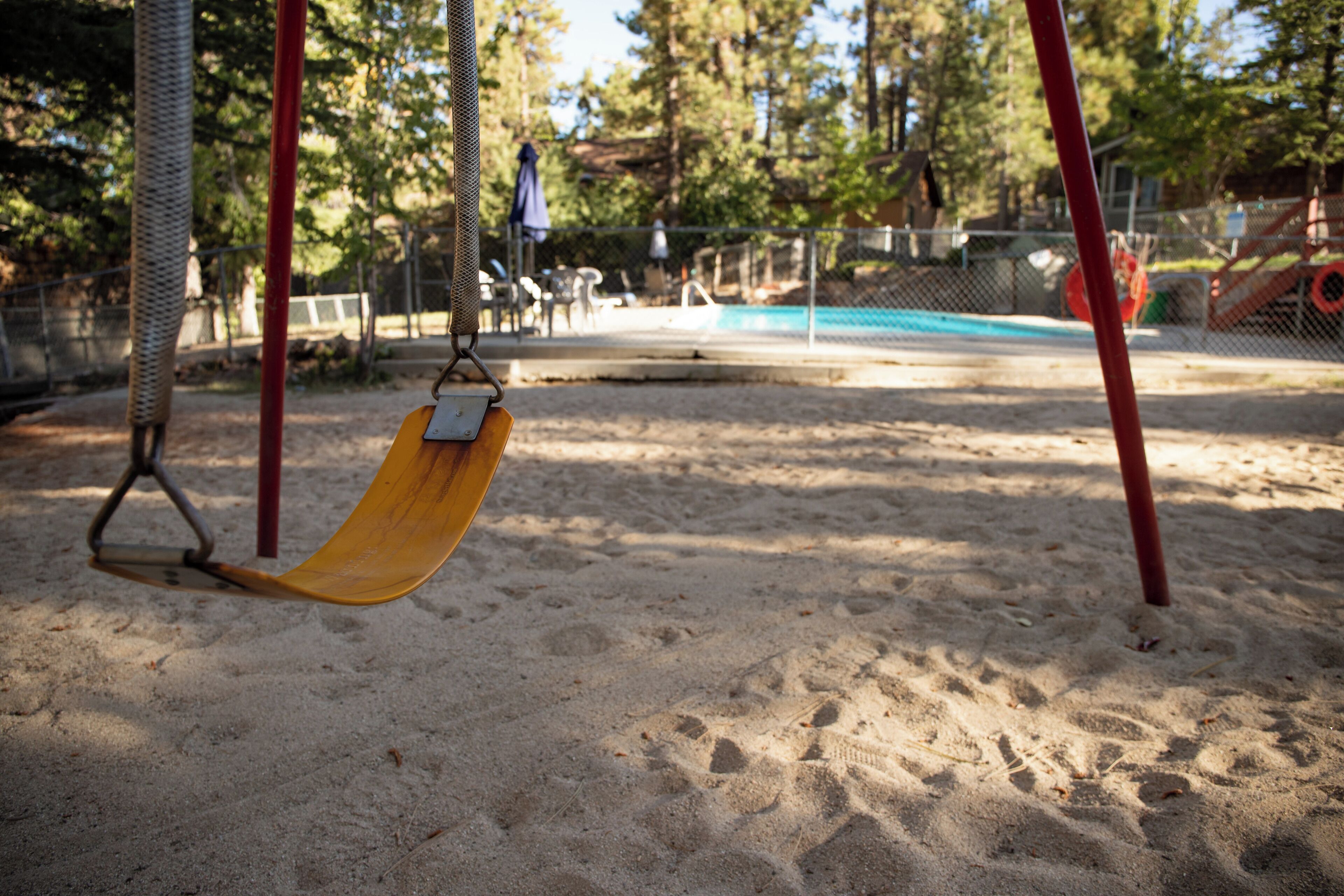 Un parque infantil con arena, una resbaladilla y una piscina cercada al fondo.