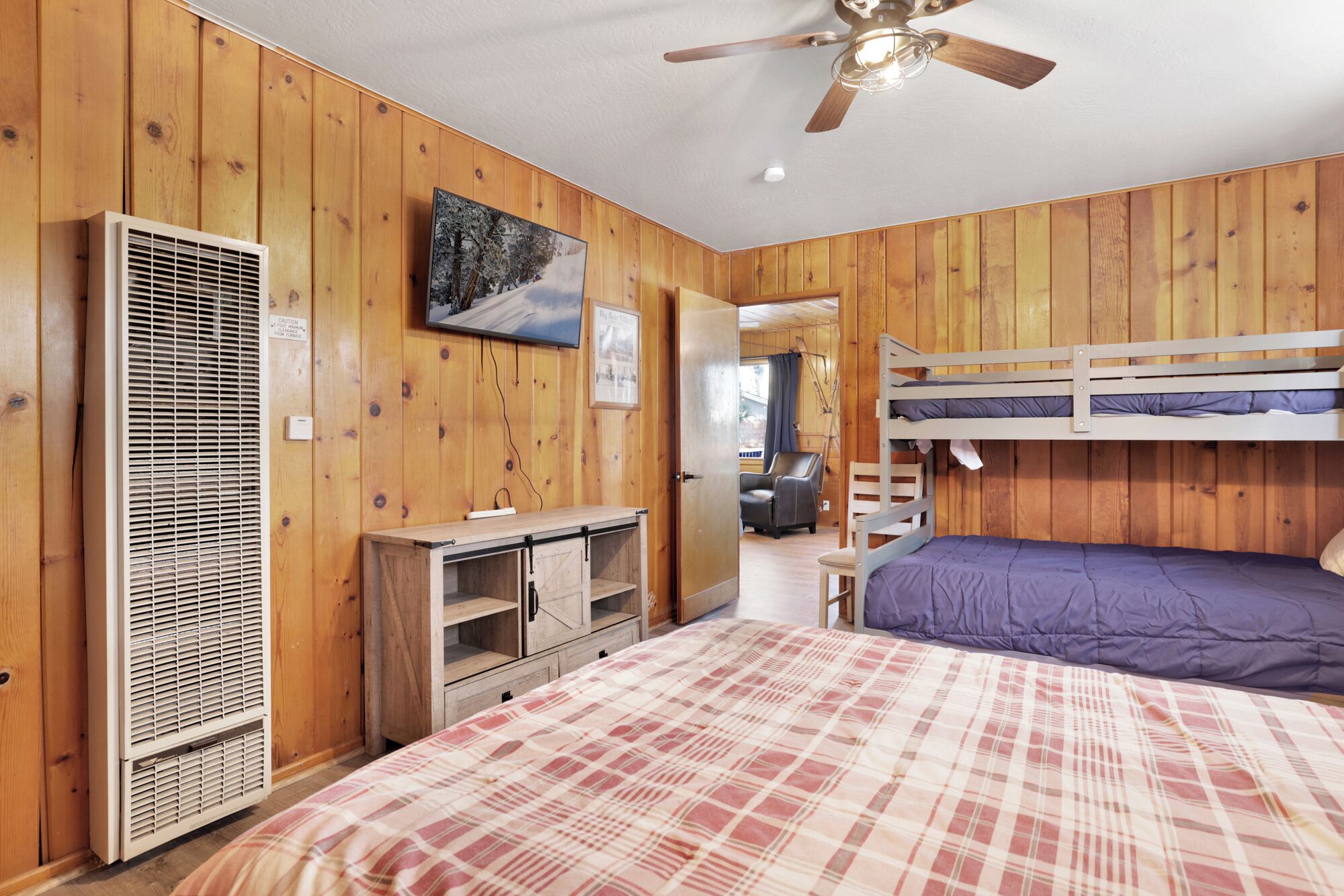 Ein Zimmer mit Holzwänden, Deckenventilator, Etagenbetten, Fernseher und Heizkörper.