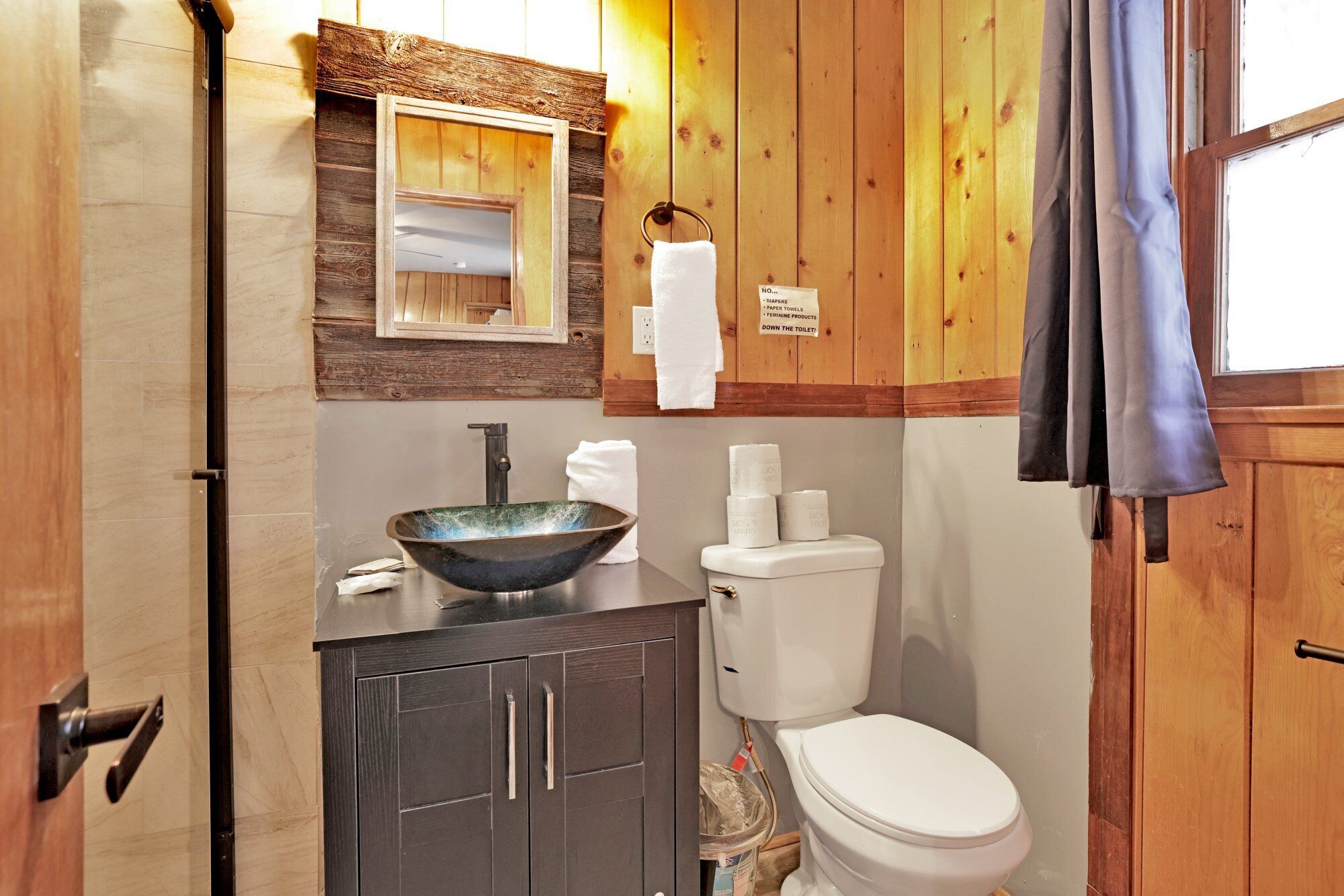 A bathroom with a wooden vanity, a large bowl sink, a toilet, and a towel rack.