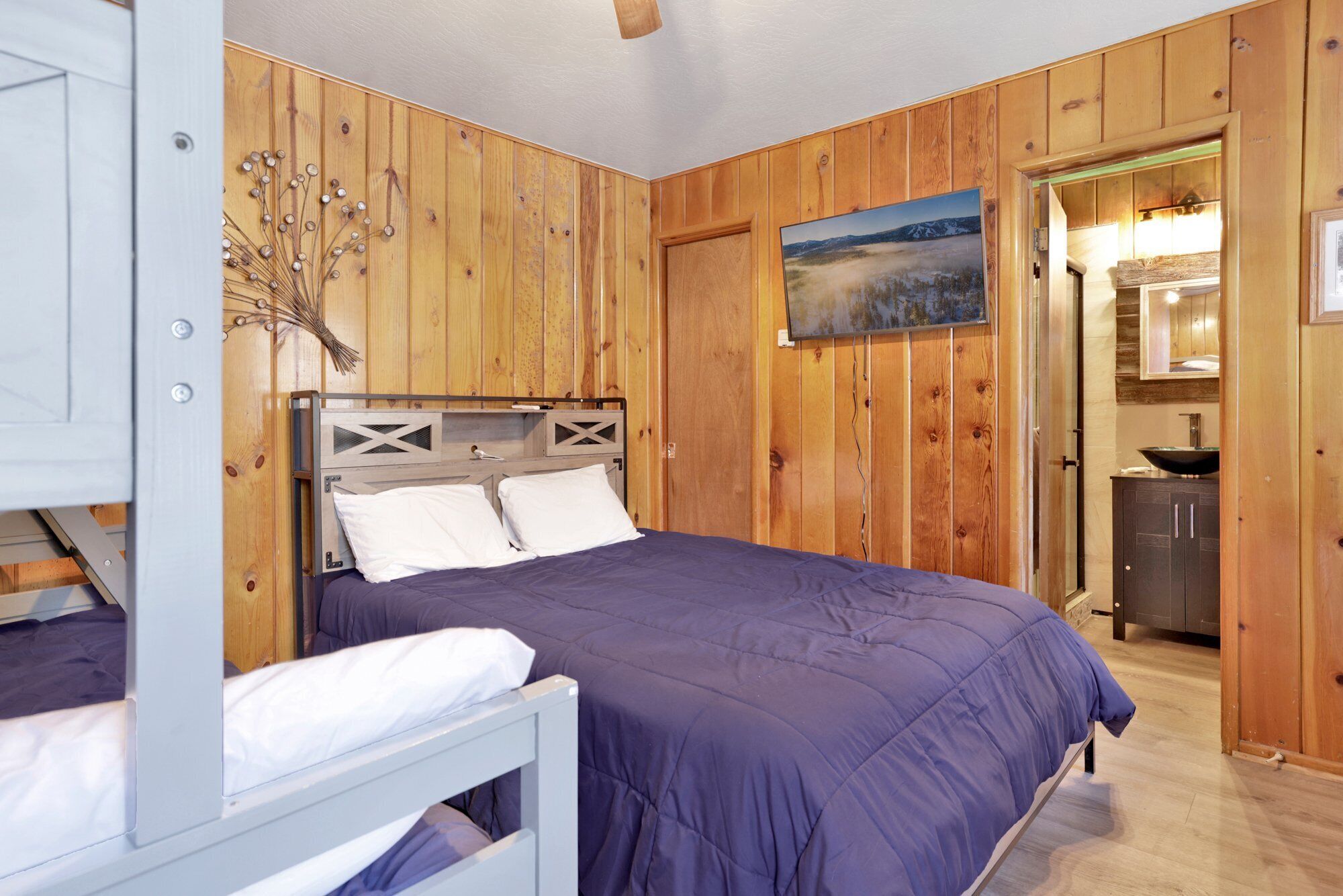 A bedroom with a bed, a nightstand, a wooden wall, a painting, and a door leading to a bathroom.