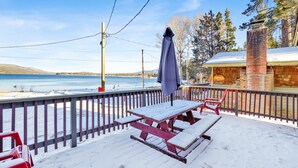 A snow-covered deck with picnic tables and chairs, overlooking a lake and a building with a sign reading "Lakefront." - Lakeside 109 (Big Bear Lake)