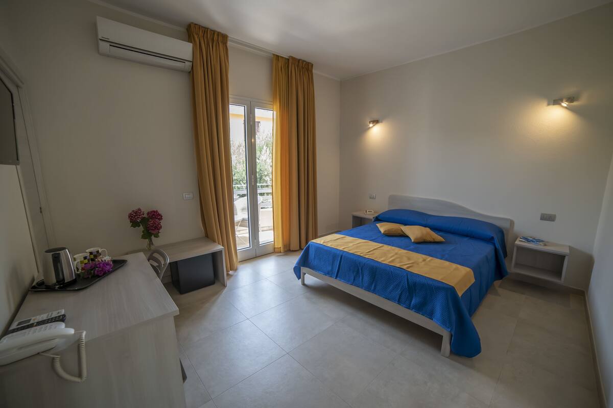 A bedroom with a bed, bedside tables, a desk with a telephone, and a window with curtains.