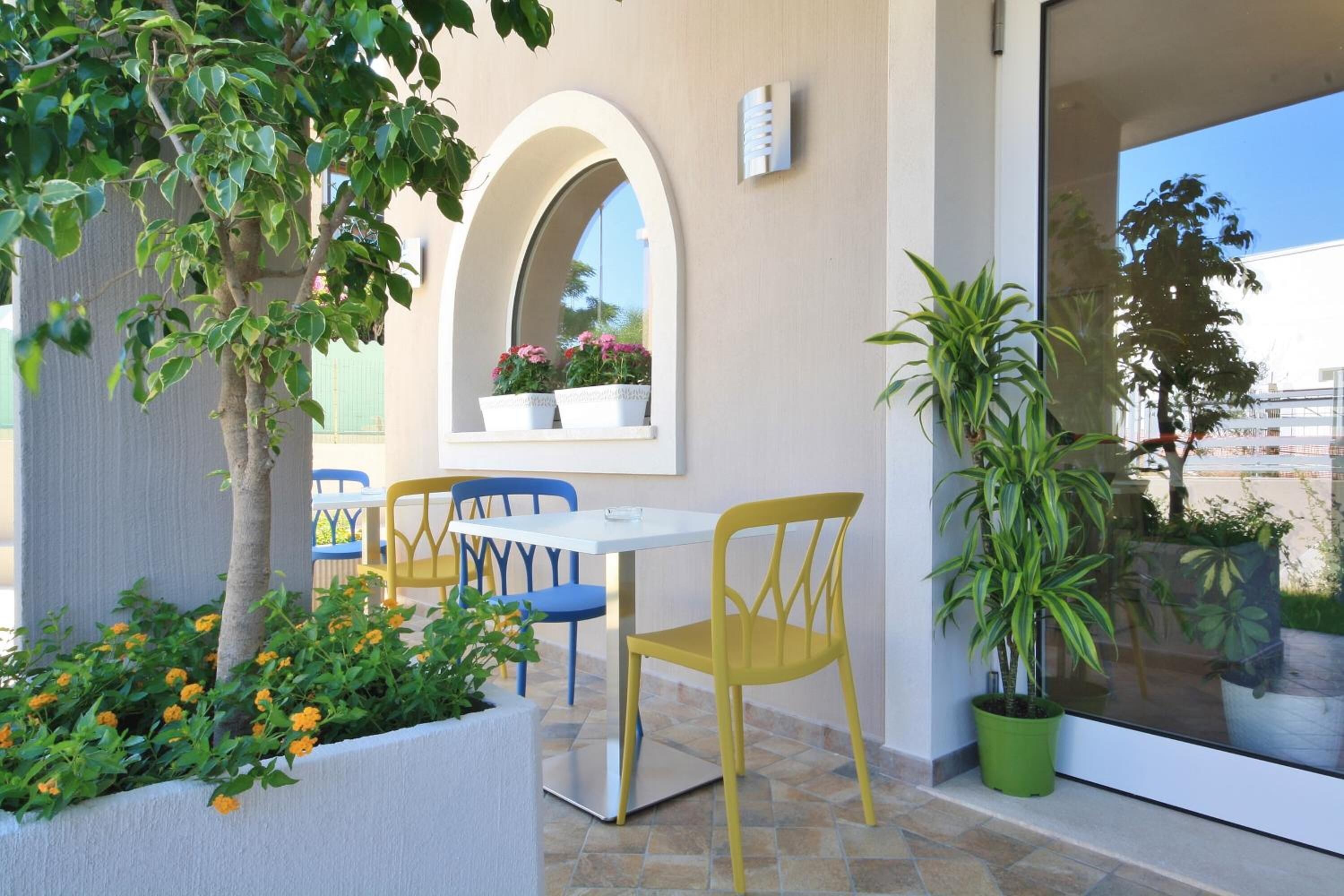 A patio area with a white table and yellow chairs, a potted plant, and a window with a view of the sky and buildings.