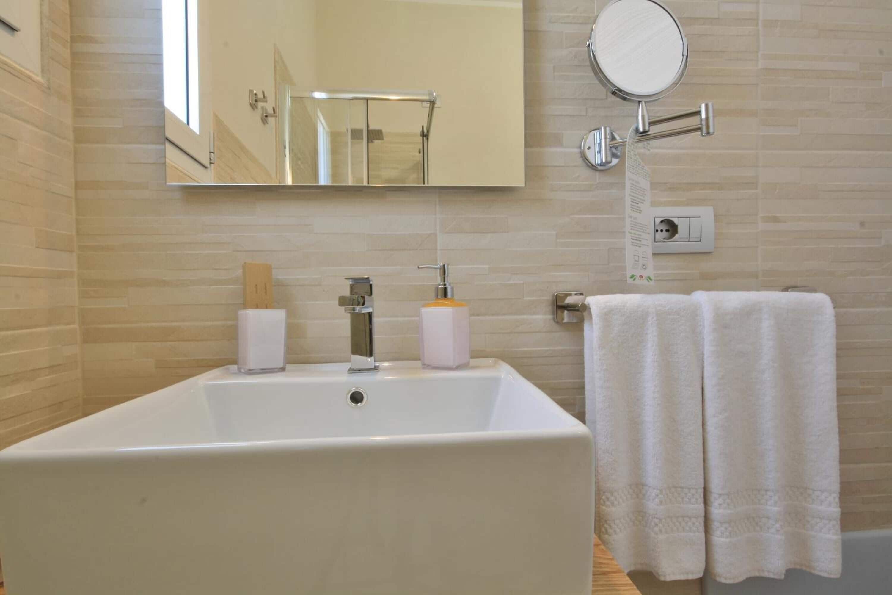 Une salle de bain avec un grand lavabo blanc, un miroir, un porte-serviettes et un luminaire fixé au mur.