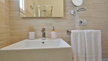 Une salle de bain avec un grand lavabo blanc, un miroir, un porte-serviettes et un luminaire fixé au mur.