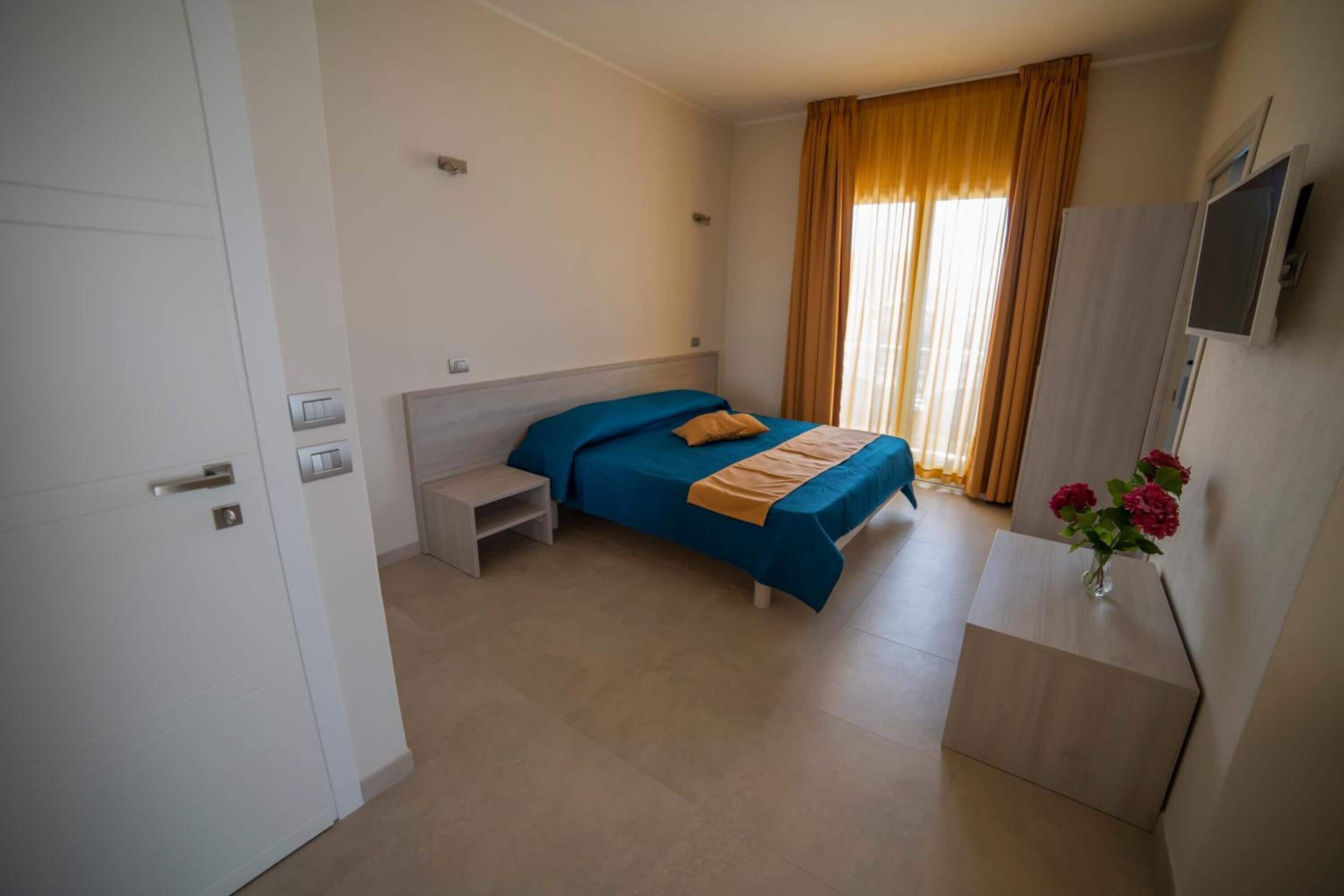 Habitación de hotel con cama, escritorio, silla, televisor y ventana con cortinas.