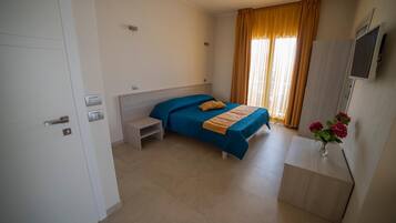 Habitación de hotel con cama, escritorio, silla, televisor y ventana con cortinas.