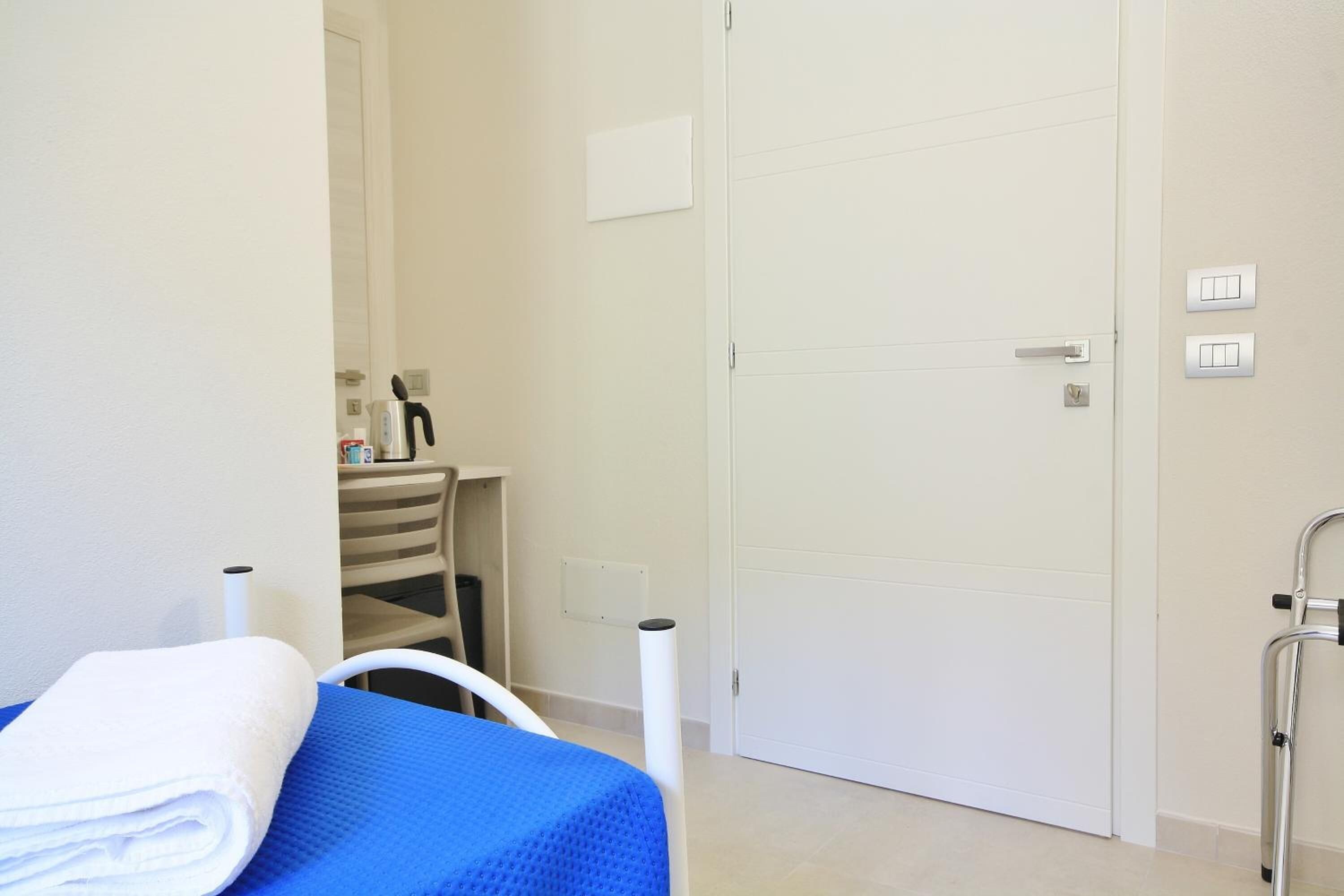 A room with a bed, a white door, a white chair, and a white towel on the bed.