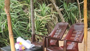 A set of plastic chairs and a small table with towels and flowers, set against a backdrop of green foliage and a bamboo structure. - Akain Villa & Holiday Home (Hikkaduwa)