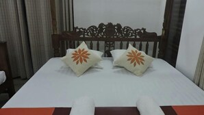 A neatly made bed with white bedding and two decorative pillows with orange floral designs. - Akain Villa & Holiday Home (Hikkaduwa)