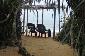 Une plage avec deux chaises en plastique placées sous une structure de toit en chaume.