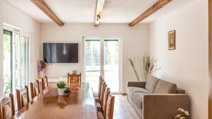 Ein Essbereich mit Holztisch und Stühlen, einer Couch, einem an der Wand montierten Fernseher und einer zur Außenwelt führenden Tür.