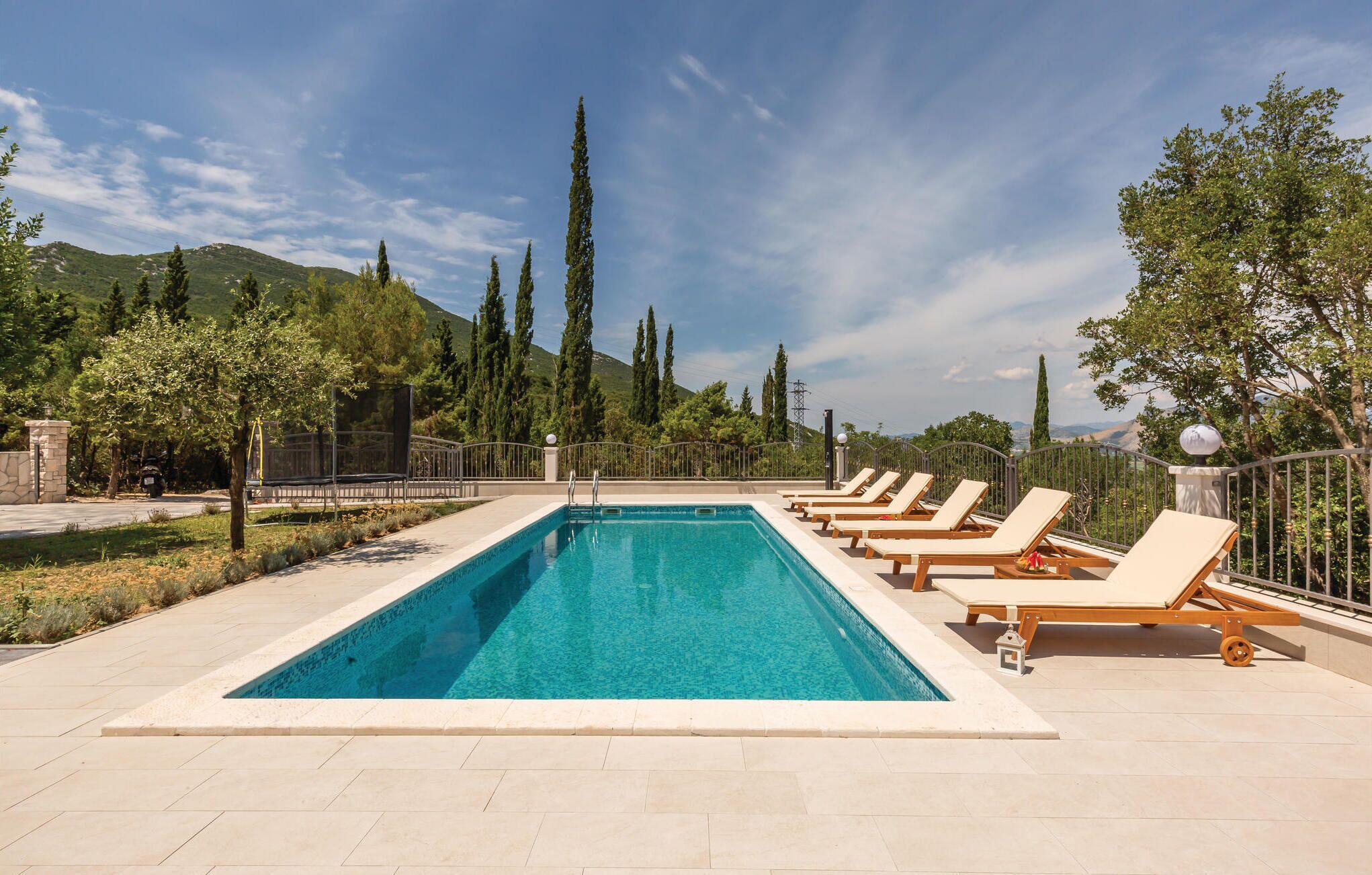 A rectangular pool with lounge chairs along the edge, surrounded by trees and a mountainous backdrop.