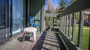 Ett trädäck med en plaststol och ett litet bord, en inglasad veranda och utsikt över en bostadsgata.