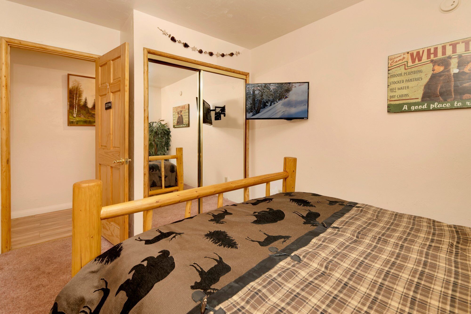 A bedroom with a bed, a wooden headboard, a wardrobe, a mirror, a television, and a poster on the wall.