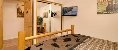 A bedroom with a bed, a wooden headboard, a wardrobe, a mirror, a television, and a poster on the wall.