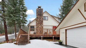 A two-story house with a stone chimney, a wooden deck, and a garage. - Swiss Delight #2244 (Big Bear Lake)