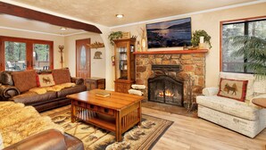 A cozy living room with a stone fireplace, leather furniture, and a large window overlooking a deck. - Swiss Delight #2244 (Big Bear Lake)