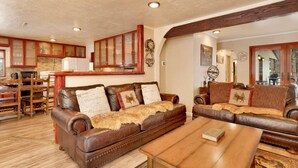 A cozy living room with a brown leather sofa, wooden coffee table, and a dining area with wooden chairs and a table. - Swiss Delight #2244 (Big Bear Lake)