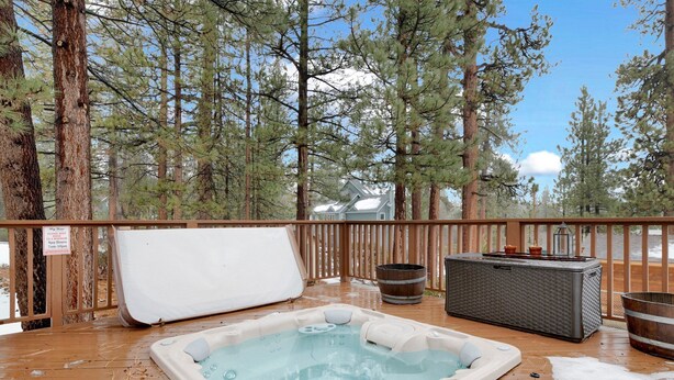 A hot tub on a wooden deck with a view of tall pine trees and a house in the background. - Swiss Delight #2244 (Big Bear Lake)