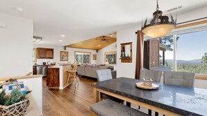 A modern kitchen with wooden cabinets, a dining area with a large island, and a view of the outdoors. - I Love View #1475 (Big Bear City)