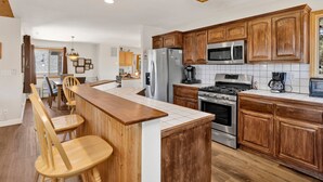 A modern kitchen with wooden cabinets, stainless steel appliances, and a central island with bar stools. - I Love View #1475 (Big Bear City)