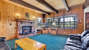 A cozy cabin interior with a fireplace, wooden walls, a sofa, and a television.