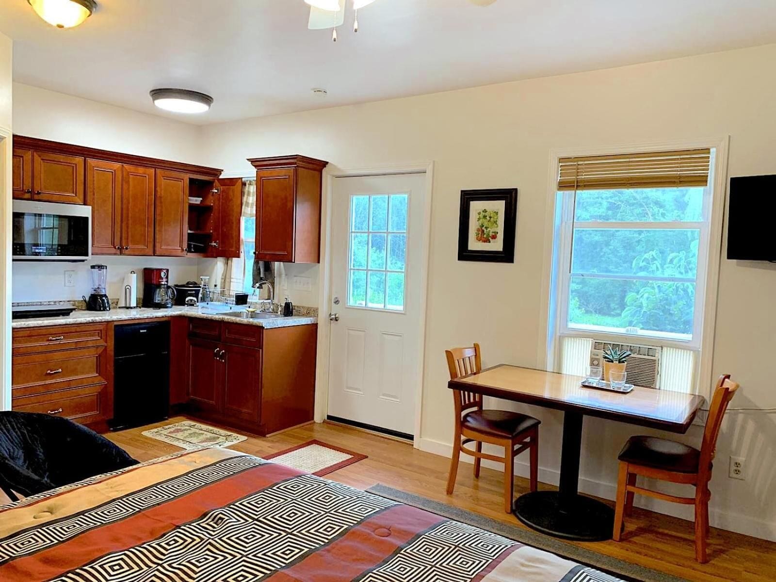Una cocina con armarios de madera, un microondas y una zona de comedor con una mesa y sillas.