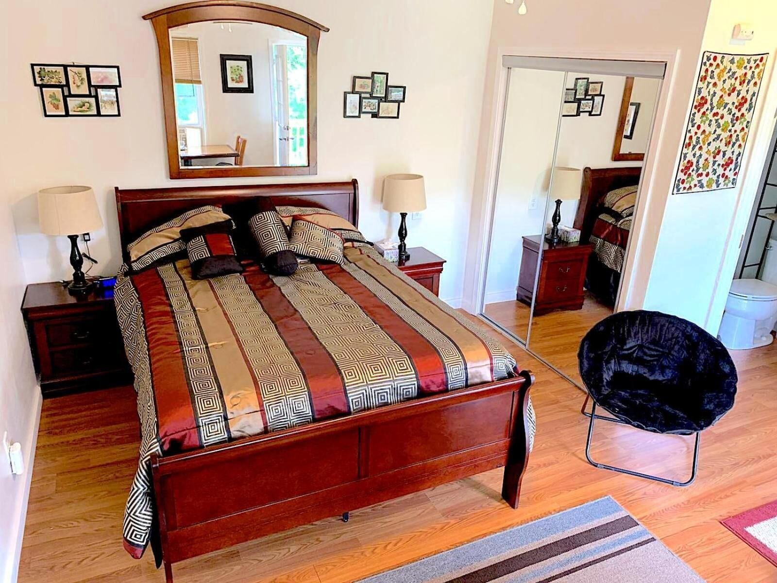Un dormitorio con una cama de madera, dos mesitas de noche, una silla negra y un espejo en la pared.