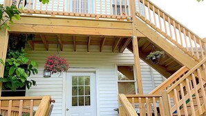 A wooden deck with a staircase leading to a porch, a white door, and hanging flower baskets.