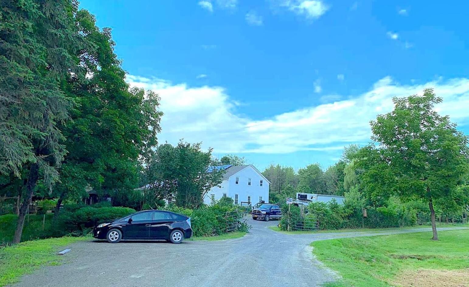 Un chemin de campagne menant à une maison blanche avec une grange, le tout entouré de verdure.