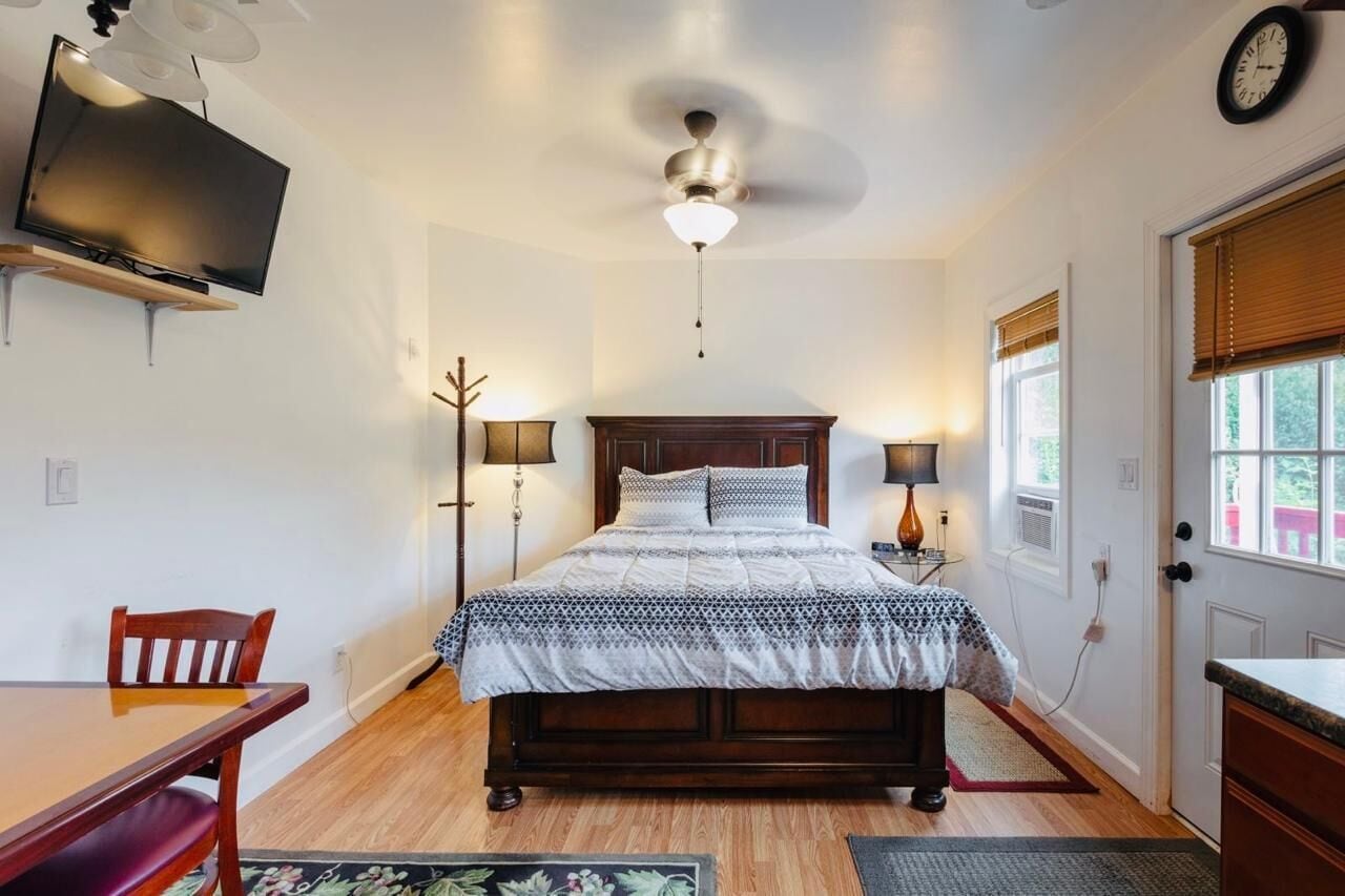 A bedroom with a bed, bedside lamps, a ceiling fan, a TV, and a clock on the wall.