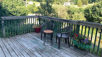Una terraza de madera con dos sillas y una mesa, rodeada por una valla verde y diversas plantas.