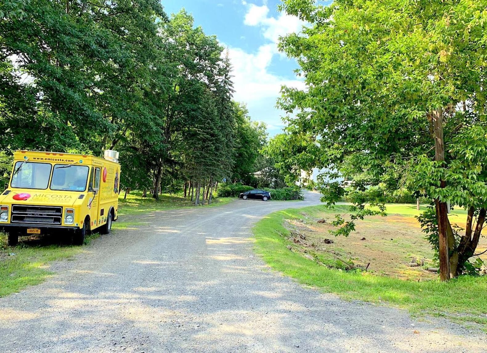 A yellow food truck parked on a gravel road surrounded by trees.
