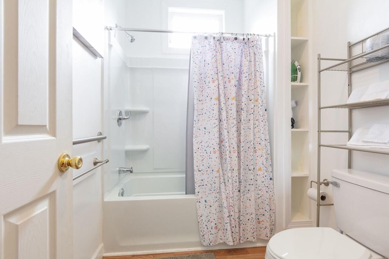 Un baño con bañera, cortina de ducha, inodoro y repisas con toallas.