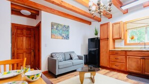 A cozy living room with a gray sofa, wooden ceiling beams, a black TV stand, and a dining area with a table and chairs.