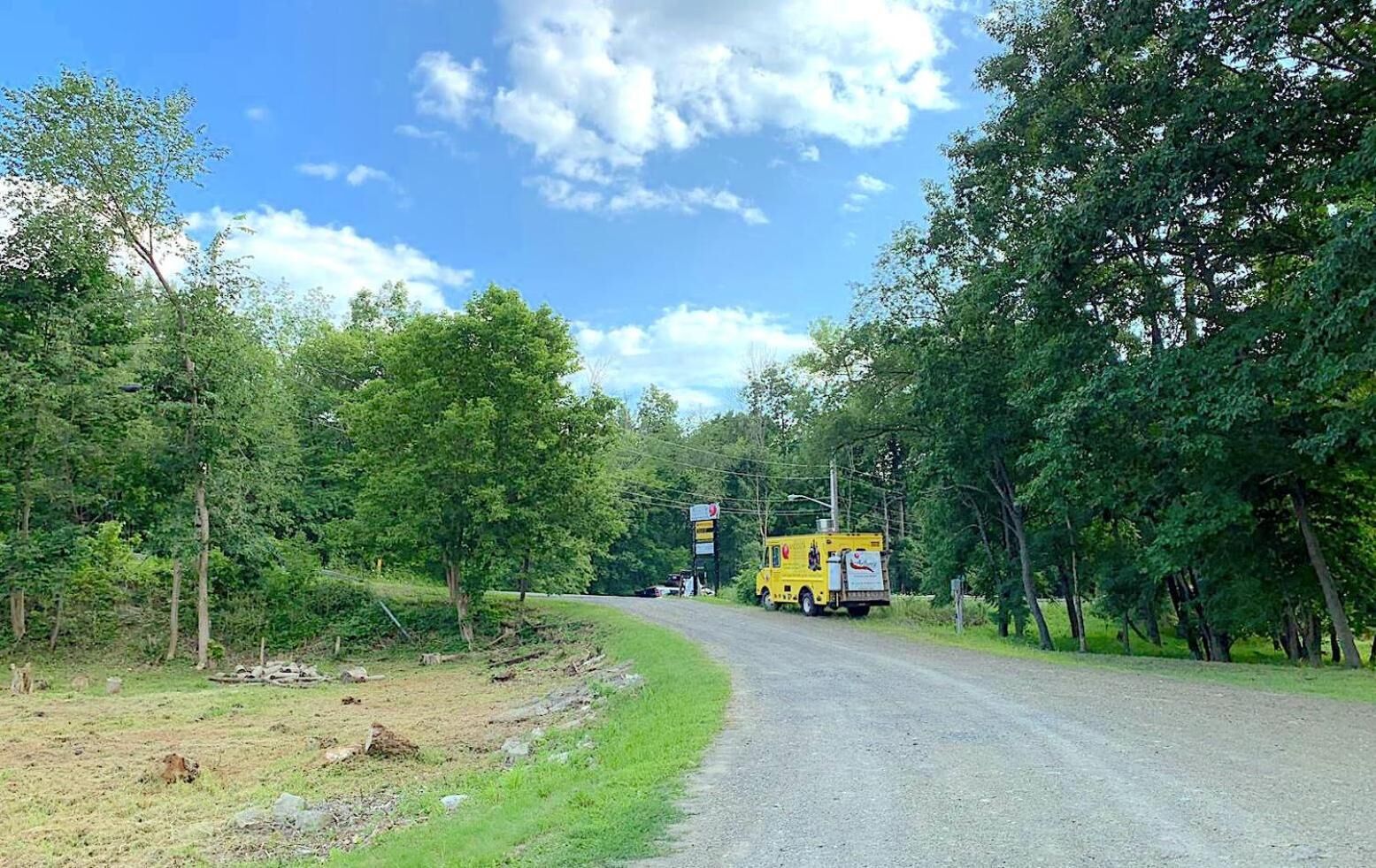 Uma estrada rural com um caminhão amarelo estacionado na lateral.
