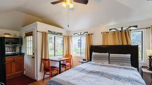 A bedroom with a bed, a desk, a chair, a ceiling fan, and a view of the outdoors.