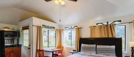 A bedroom with a bed, a desk, a chair, a ceiling fan, and a view of the outdoors.
