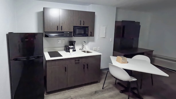 Cocina compacta con refrigerador, microondas, pileta y un pequeño comedor con una silla.