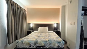 Habitación de hotel con cama, cortinas, cabecero, lámparas de noche, mesitas de noche y televisor.