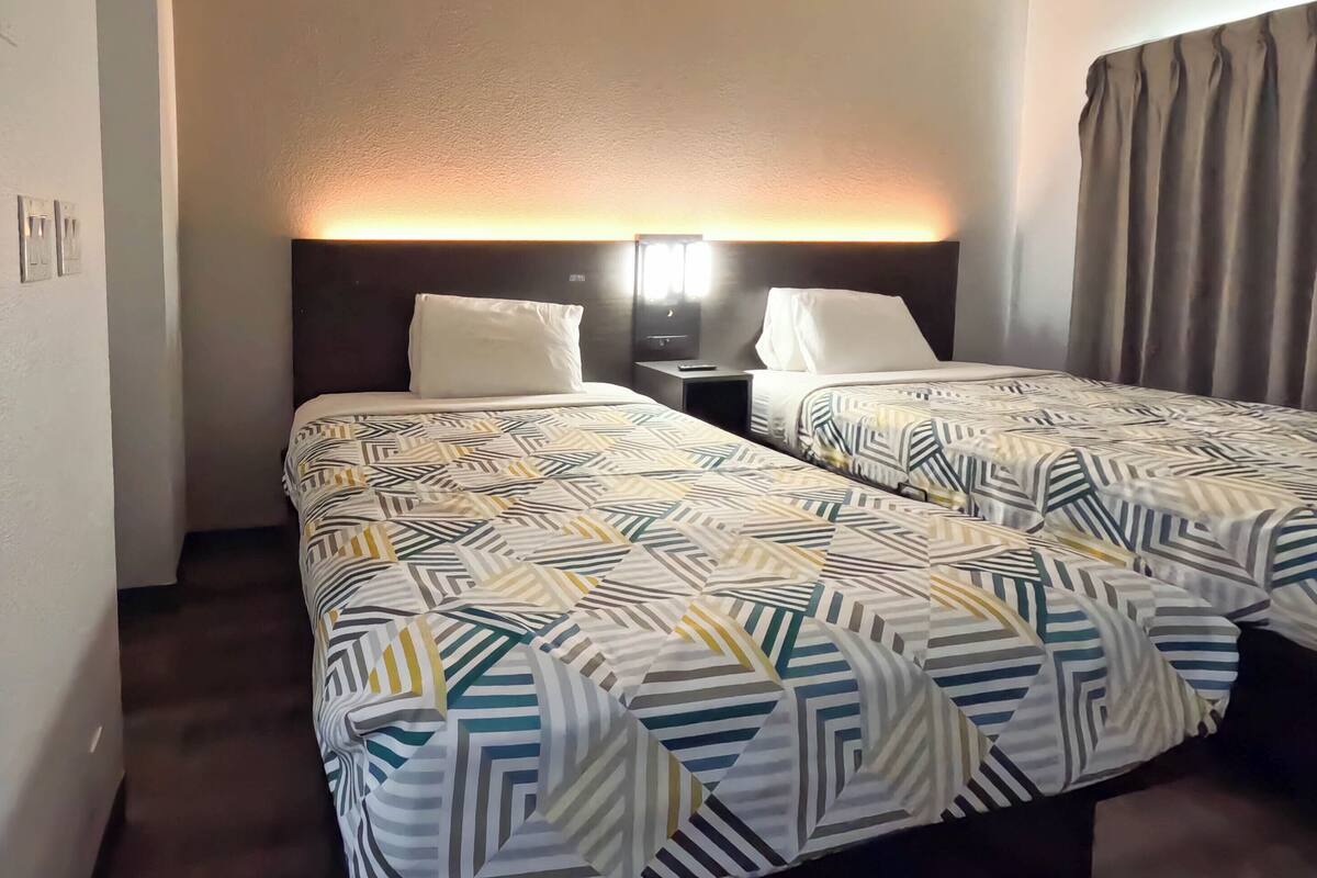 Une chambre d’hôtel avec deux lits, une table de chevet, une lampe et un rideau.