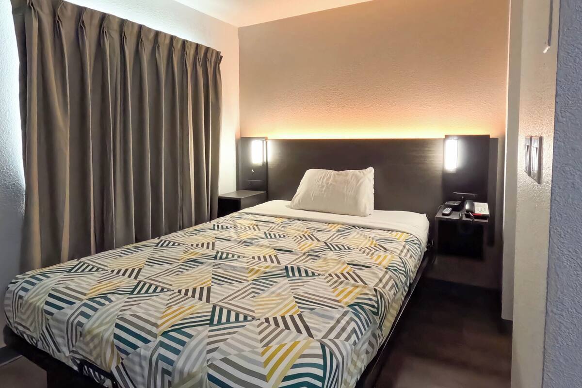 Une chambre d’hôtel avec un lit, des rideaux, une table de chevet et une lampe fixée au mur.