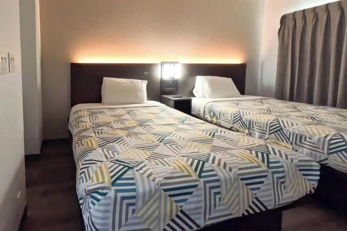 Une chambre d’hôtel avec deux lits, chacun agrémenté d’une literie à motifs, d’une table de chevet et d’une lampe fixée au mur.