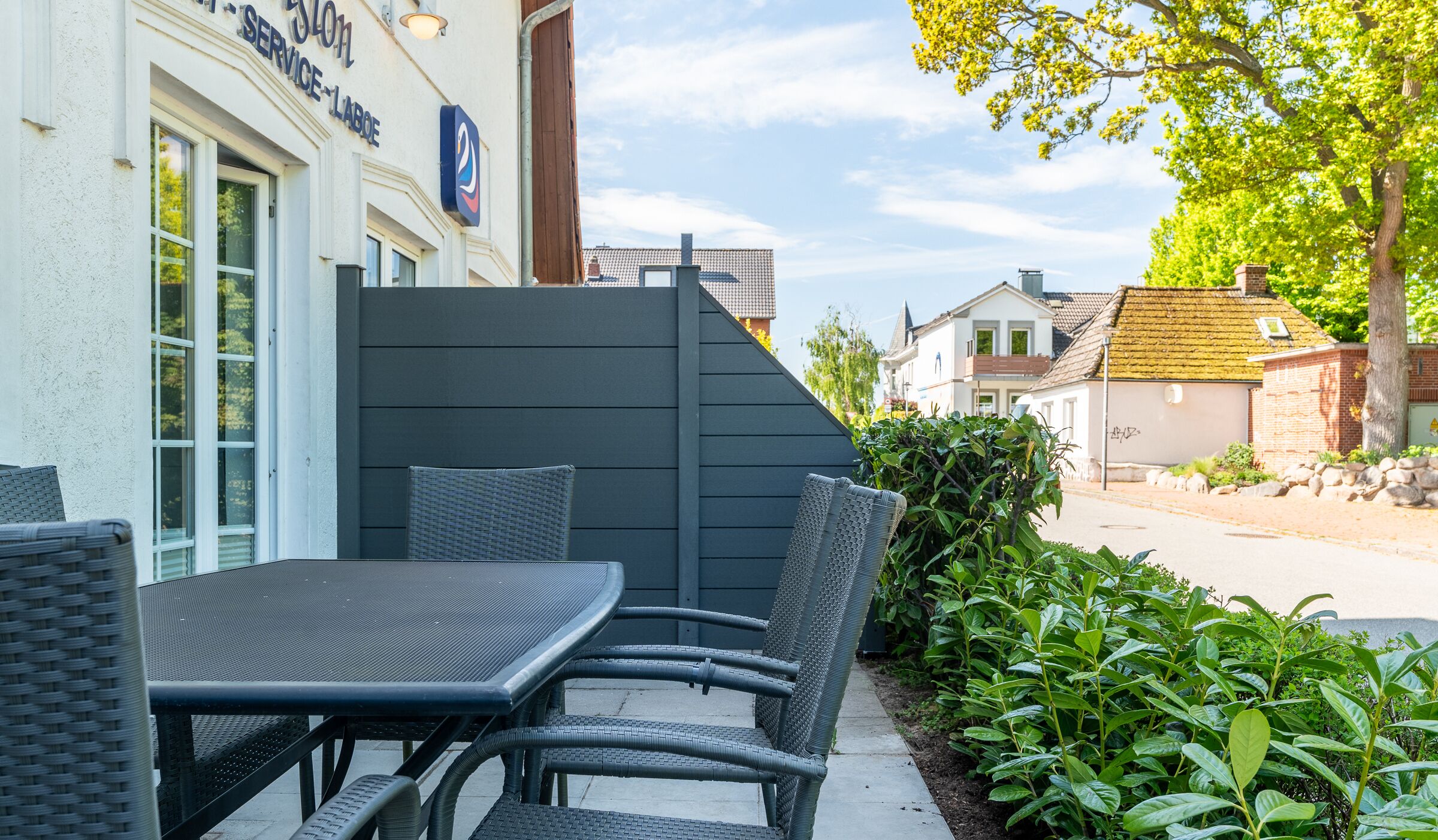 An outdoor patio with a table and chairs, a privacy screen, and a building with a sign.